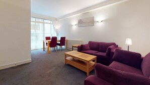 Een moderne woonkamer met een paarse bank, een houten salontafel en een eethoek met rode stoelen.