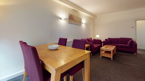 Een kamer met een houten tafel en paarse stoelen, een paarse bank en een klein houten bijzettafeltje.