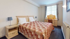 Een slaapkamer met een bed, nachtkastjes, een bureau en een stoel.