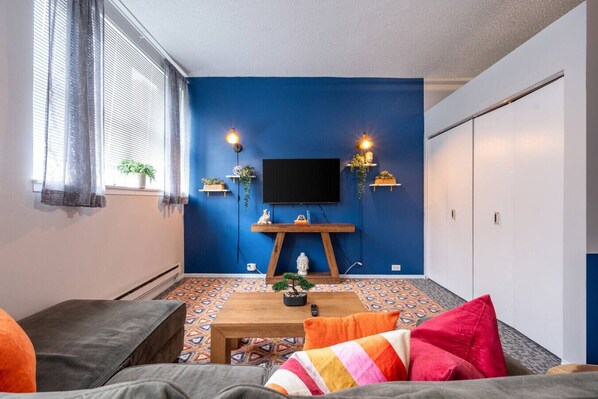 Quarto com parede azul decorativa, televisão montada, mesa de madeira e piso estampado.