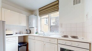 Een keuken met witte kasten, een fornuis, een spoelbak en een raam met jaloezieën.