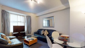 Een moderne woonkamer met een bank, een glazen salontafel, een televisie en een eethoek met een glazen tafel en stoelen.