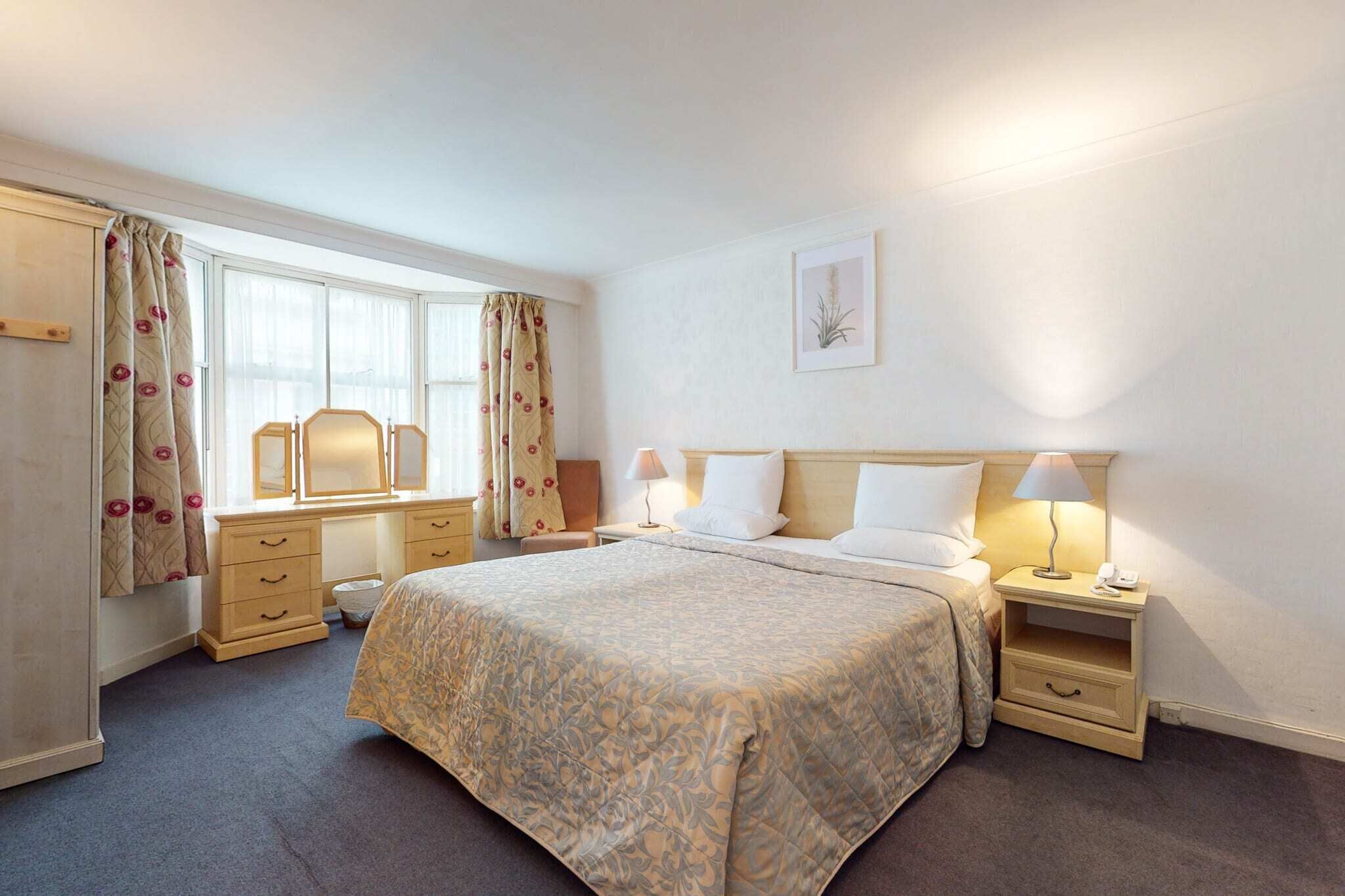 A hotel room with a large bed, bedside tables with lamps, a dresser, and a window with curtains.