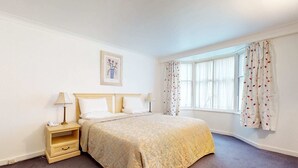 Ein ordentlich eingerichtetes Schlafzimmer mit einem Bett, Nachttischen und einem Fenster mit Vorhängen.