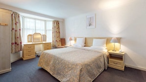 A hotel room with a large bed, bedside tables with lamps, a dresser, and a window with curtains. - Luxury Serviced Apartment, Staffed Reception, Two Bathrooms, Large Living Room a (London)