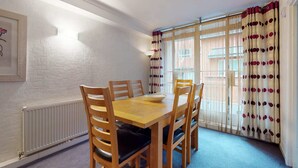 A dining area with a wooden table and chairs, a white radiator, and a window with patterned curtains. - Luxury Serviced Apartment, Staffed Reception, Two Bathrooms, Large Living Room a (London)