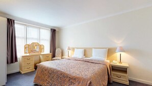 Hotellihuone, jossa on suuri sänky, kaksi yöpöytää valaisimineen, lipasto ja ikkuna, jossa on verhot.
