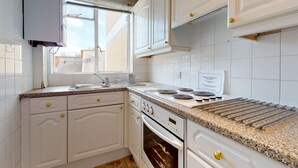 Una cucina con mobili bianchi, un piano di lavoro in granito, un forno integrato e una finestra.