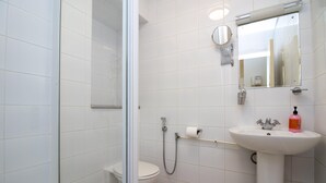 Un bagno con box doccia in vetro, un water, un lavandino con specchio e un dispenser di sapone.