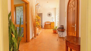 A hallway with a wooden door, a potted plant, a wooden bench, and a wall-mounted lamp.