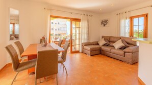 A spacious living area with a dining table, chairs, a sofa, and a large window.