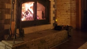 Una chimenea de piedra con fuego, paredes de madera y techo de madera.