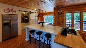 Una cocina moderna con vigas de madera, una isla central con taburetes, un refrigerador y una zona de bar.