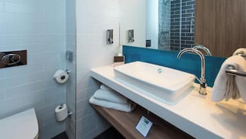 A modern bathroom with a white sink, a glass shower enclosure, and a wooden vanity.