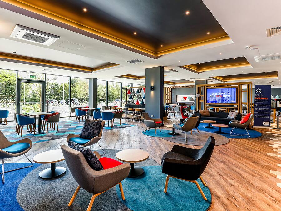 A modern hotel lobby with a variety of seating options, a large TV screen, and a view of the outdoors.