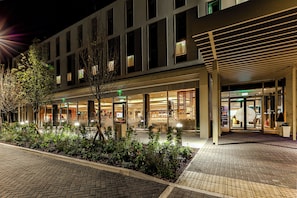 Une entrée d’hôtel moderne avec un chemin en briques, un jardin aménagé et une façade en verre.