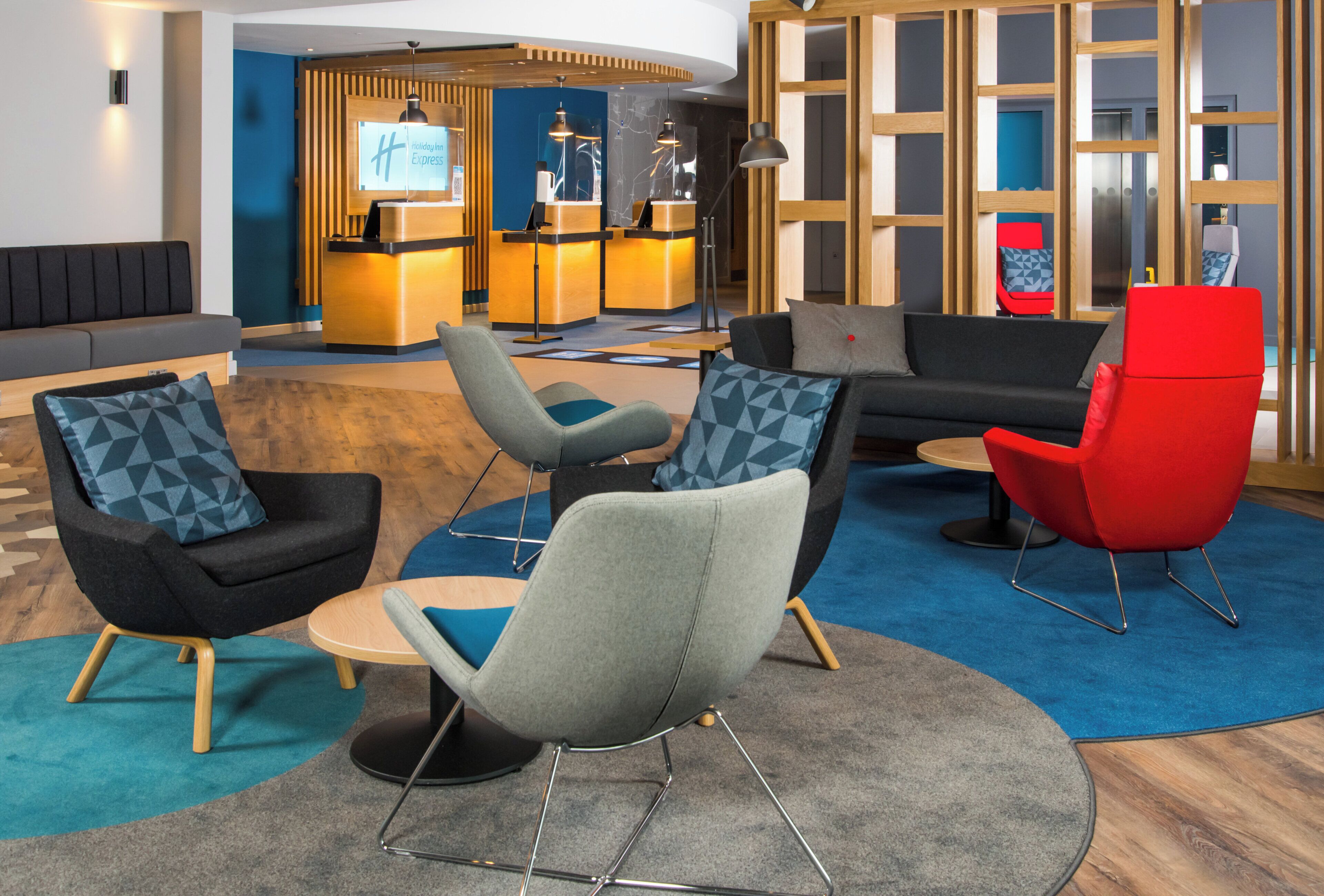 A modern hotel lobby with a reception desk, seating area, and a large window.