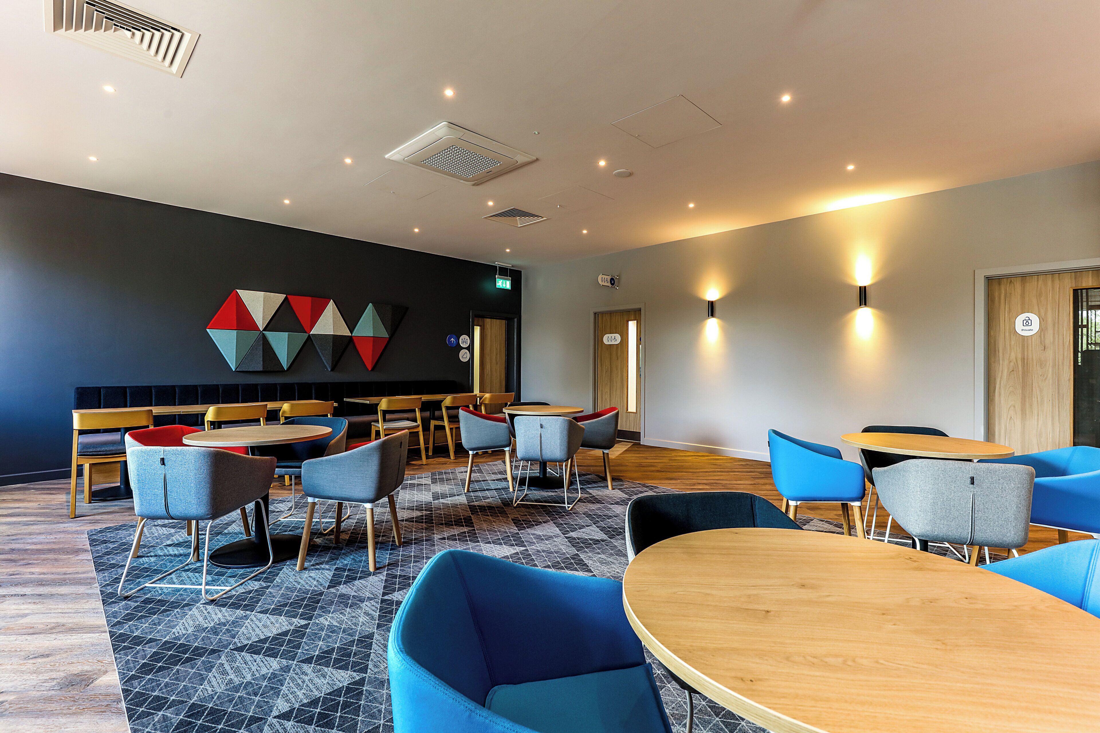 A modern interior with round tables and chairs, a geometric wall art piece, and a patterned carpet.