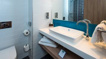 A modern bathroom with a white sink, a glass shower enclosure, and a wooden vanity.