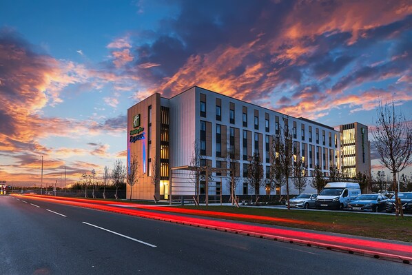 A modern hotel building with a prominent sign, a parking lot, and a clear sky. - Holiday Inn Express Bicester by IHG (Bicester)