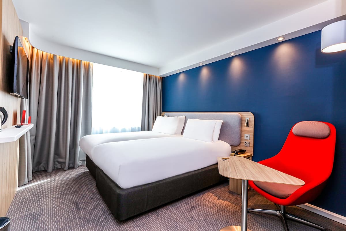 A hotel room with a large bed, a desk, a chair, and a TV.