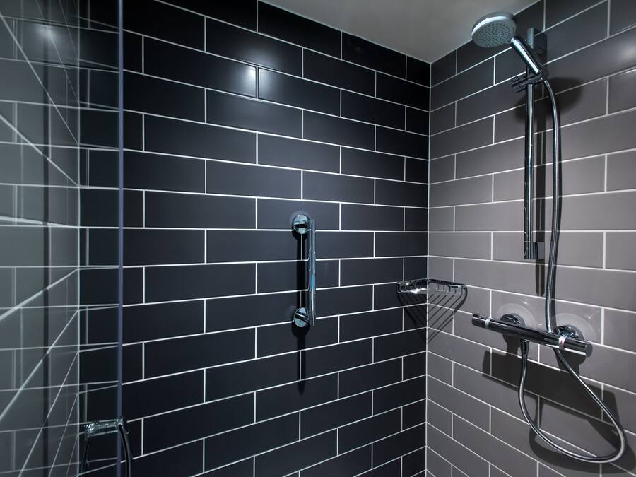 A bathroom with black tiled walls, a shower, and a handheld showerhead.