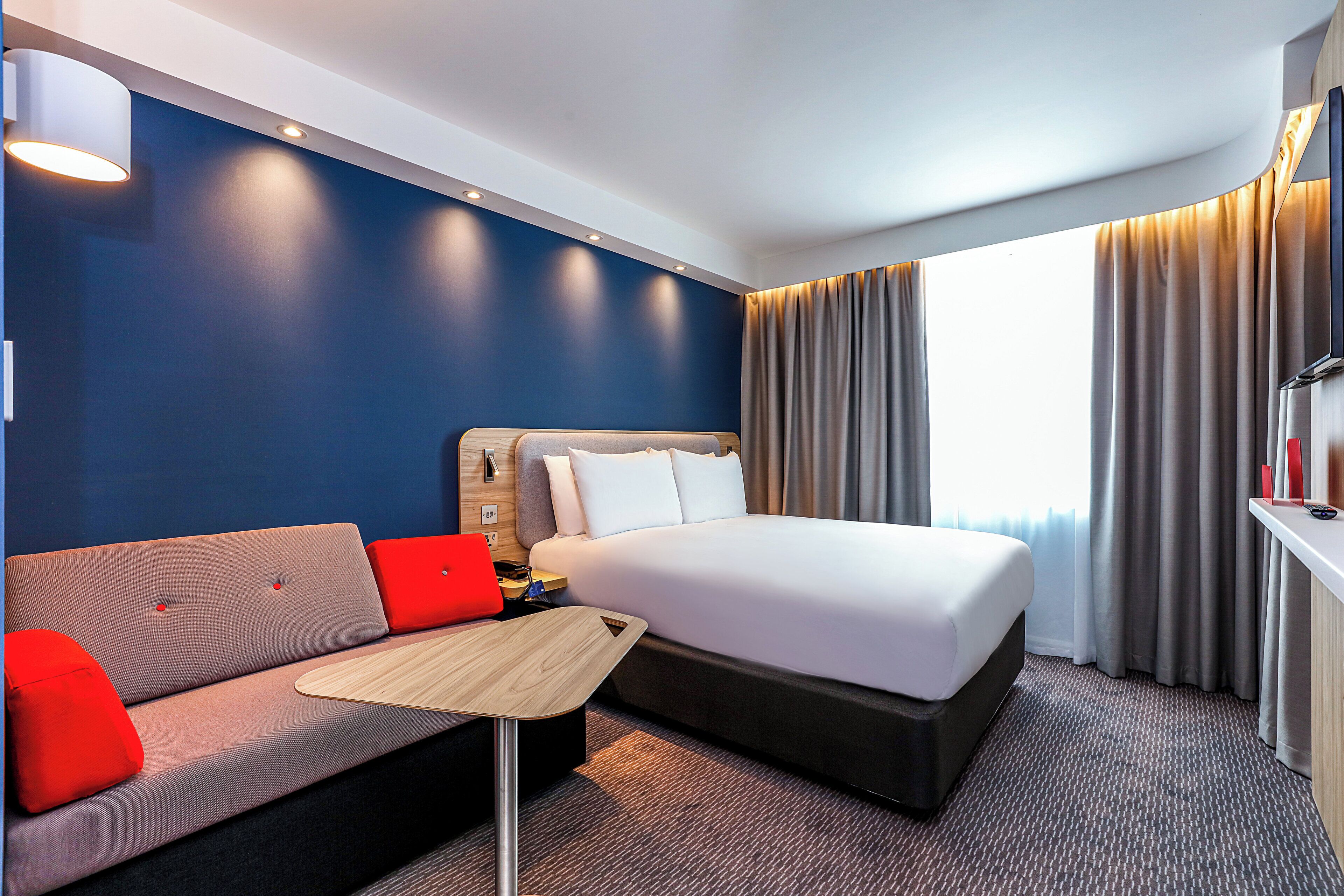 A hotel room with a bed, a sofa, a small table, and a TV on a stand.