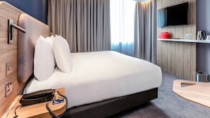 A modern hotel room with a large bed, a mounted TV, a bedside table with a phone, and a small desk area. - Holiday Inn Express Bicester by IHG (Bicester)