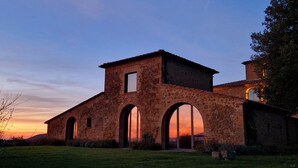 Un edificio in pietra con finestre ad arco e una torre centrale, immerso in un'area verde.