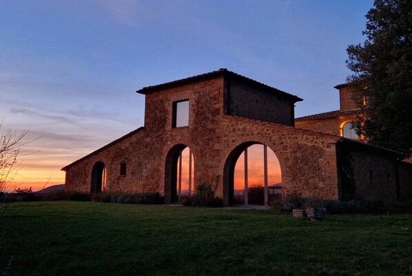 A stone building with arched windows and a central tower, surrounded by a grassy area.
