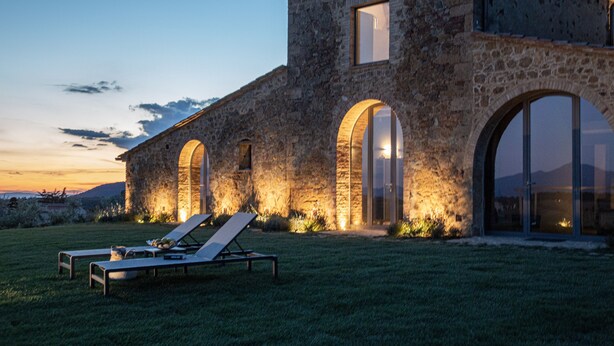 Un edificio in pietra con ampie finestre ad arco e un ingresso ben illuminato. In primo piano, due poltrone da relax.