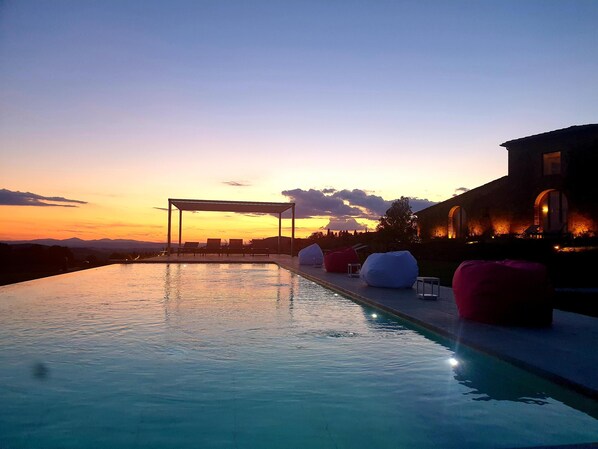 An infinity pool with lounge chairs and bean bags, set against a sunset backdrop. - Authentic Tuscan Villa with infinity pool & stunning views of Val d'Orcia (Montefollonico)