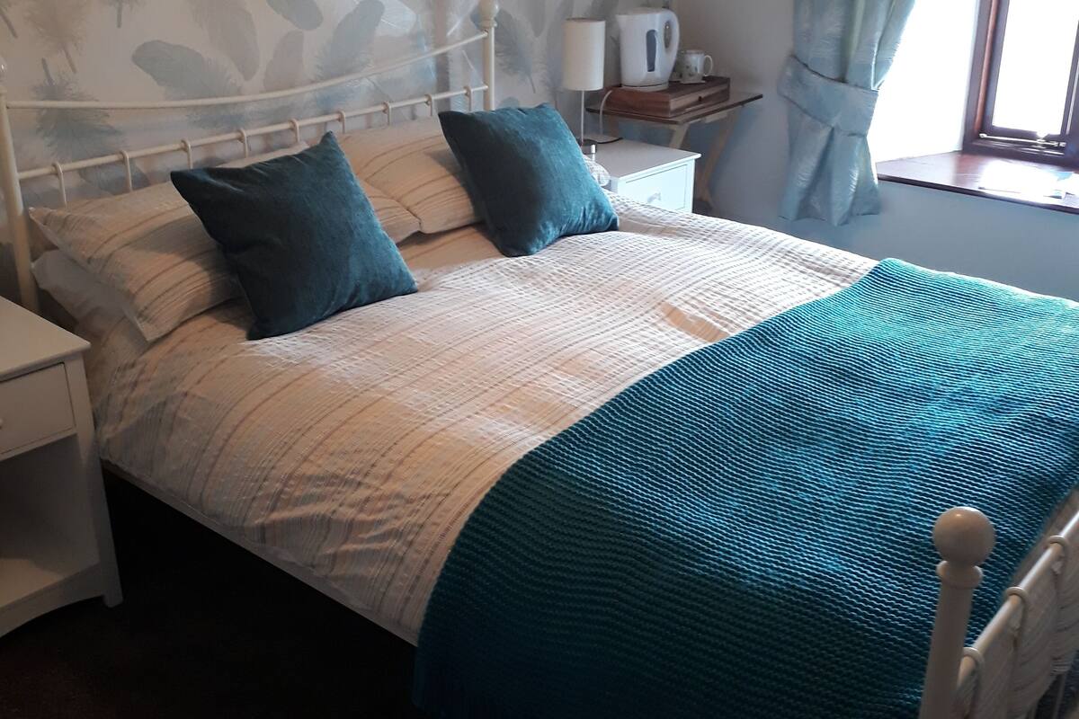 A neatly made bed with a patterned headboard, a bedside table with a lamp, and a window with curtains.