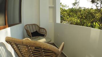 Un balcón con sillas de mimbre y una mesa de vidrio, con vista a un jardín exuberante.