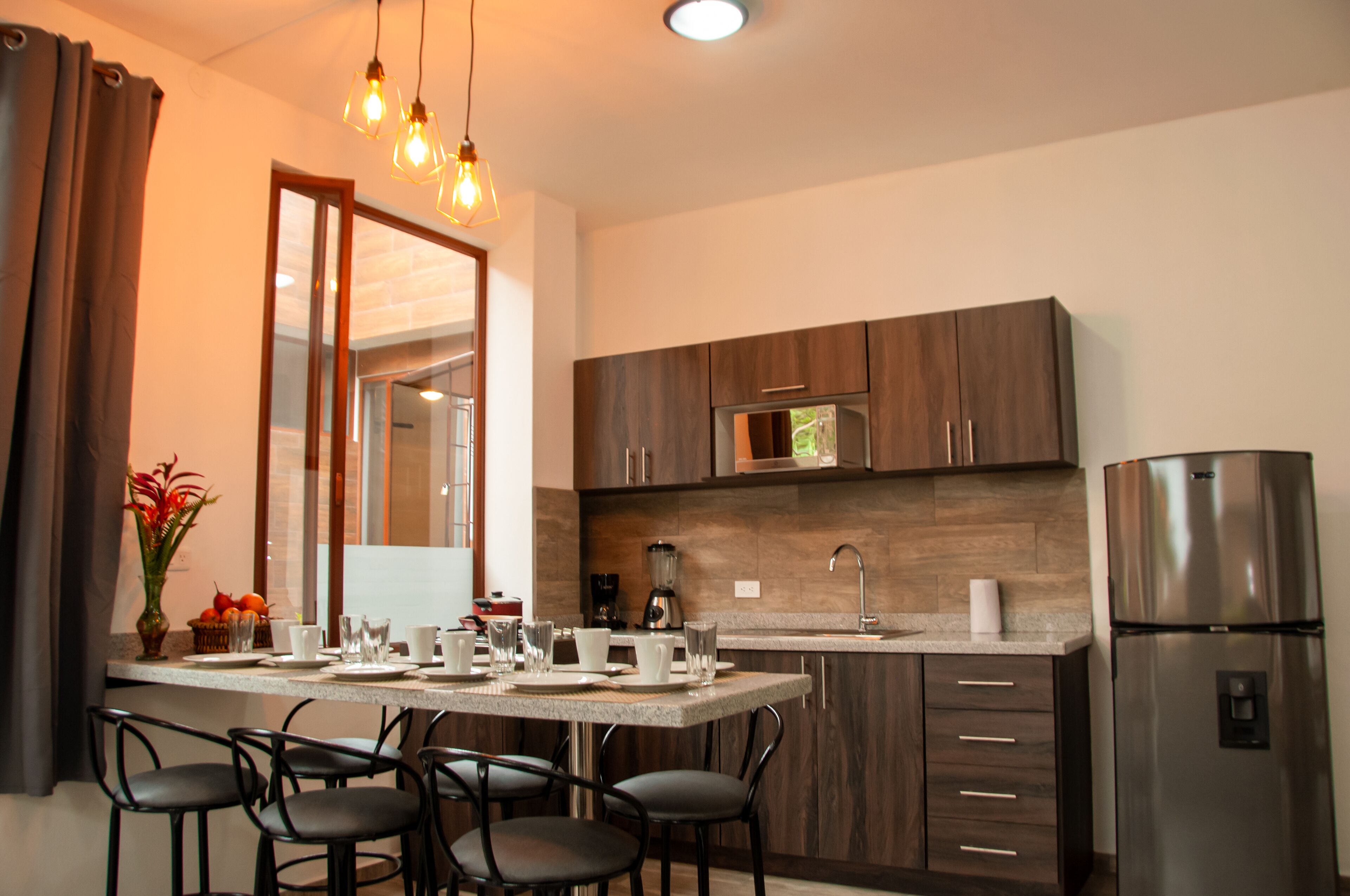 A modern kitchen with dark wooden cabinets, a stainless steel refrigerator, a built-in microwave, and a dining area with a table and chairs.