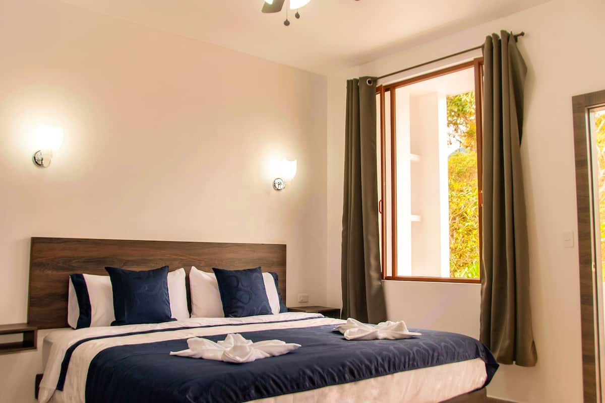 A neatly made bed with a wooden headboard, two bedside lamps, and a window with curtains.