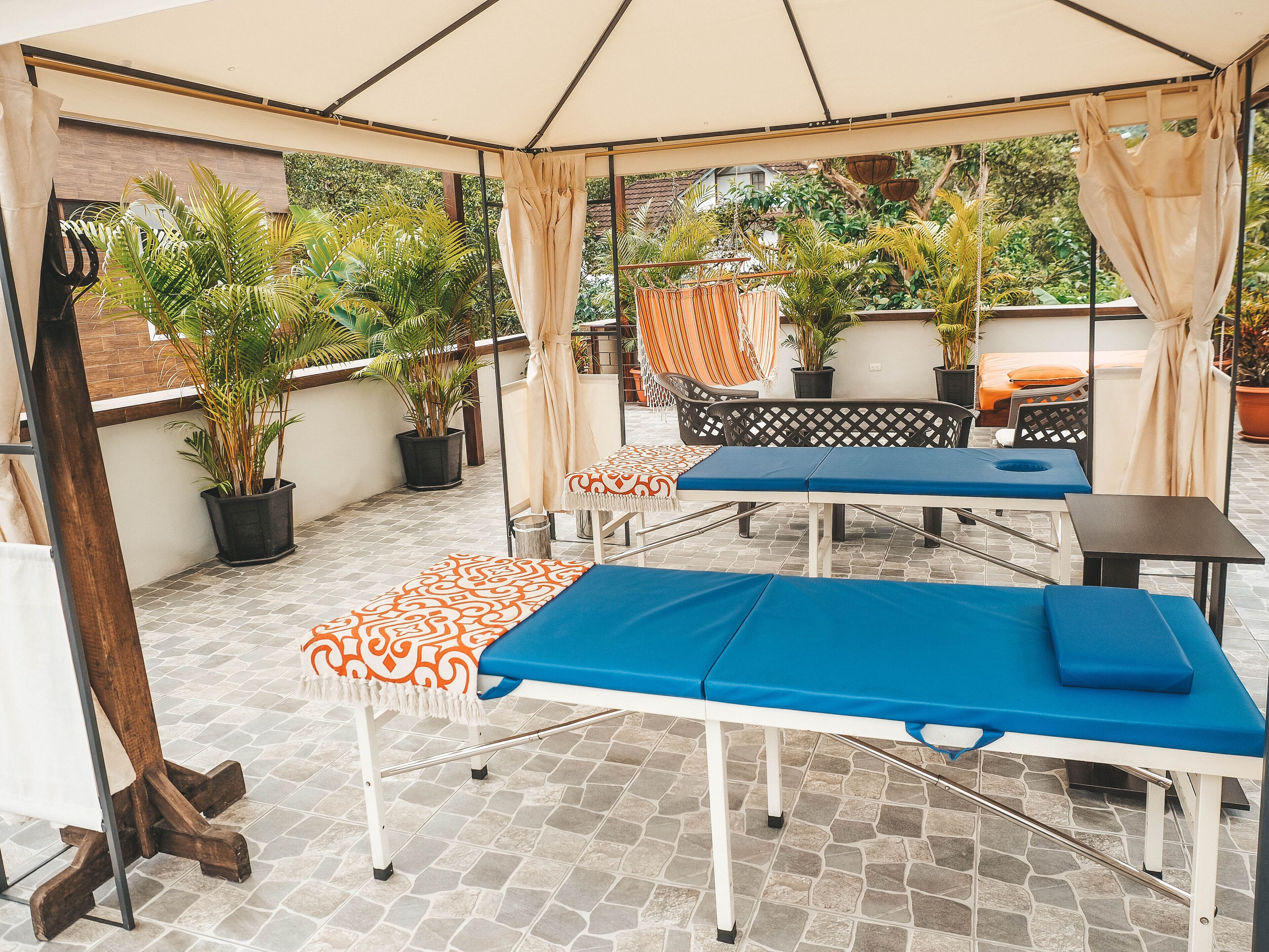 Un espacio al aire libre cubierto con una mesa de masajes, sillones de descanso y plantas en macetas.