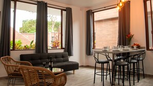 A modern living room with a sofa, dining table, chairs, and large windows with curtains. - Toucan Platinum Suites Aparthotel (Mindo)