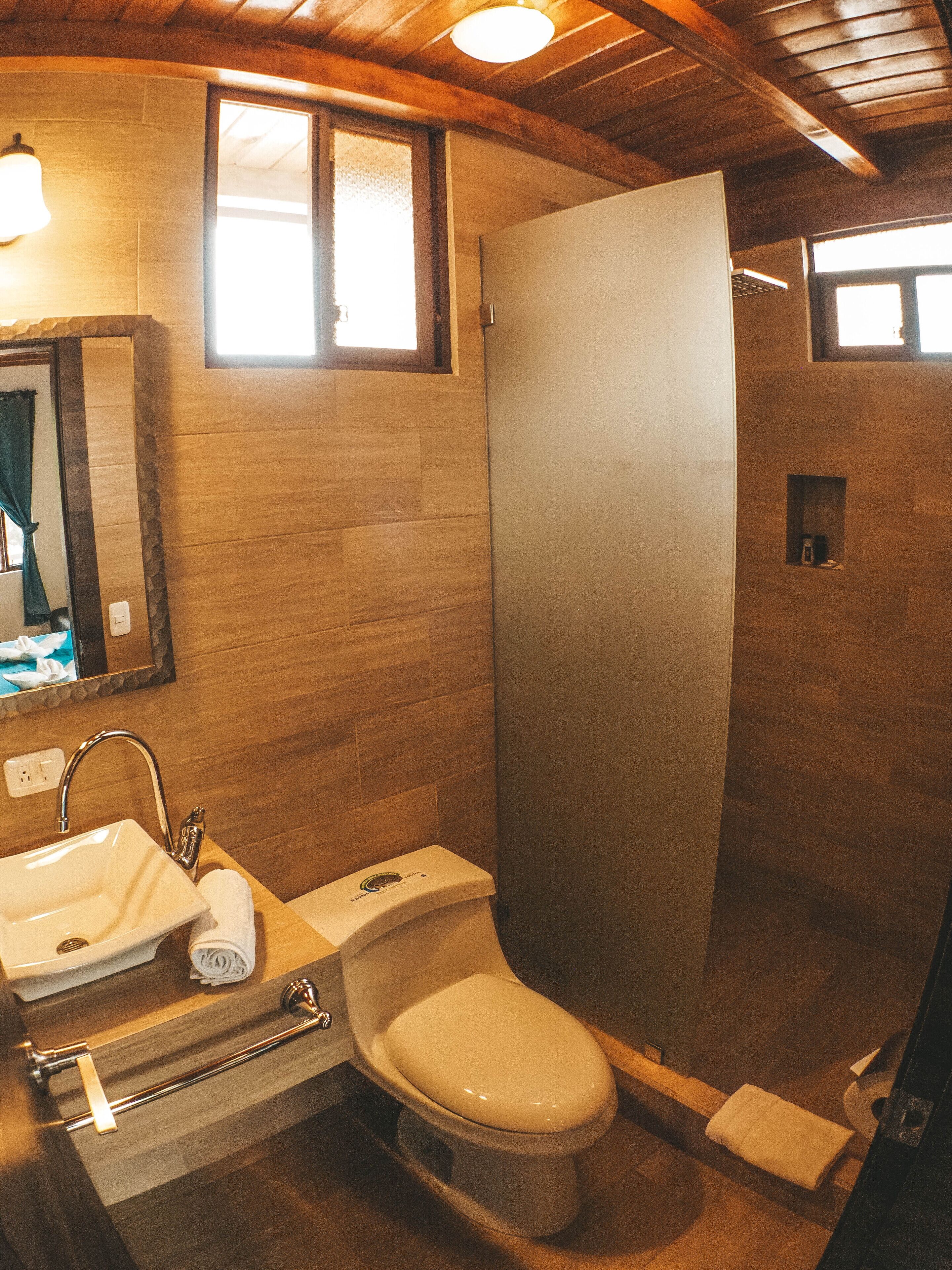 A bathroom with a wooden ceiling, a sink, a toilet, and a shower stall.