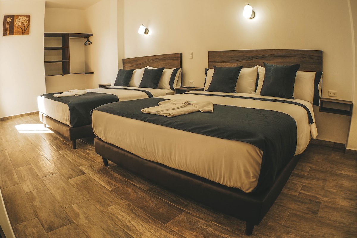 A hotel room with two beds, wooden flooring, and wall-mounted light fixtures.