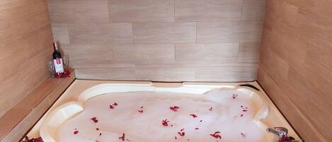 A bathtub filled with water and rose petals, with a wine bottle and glasses on the side.