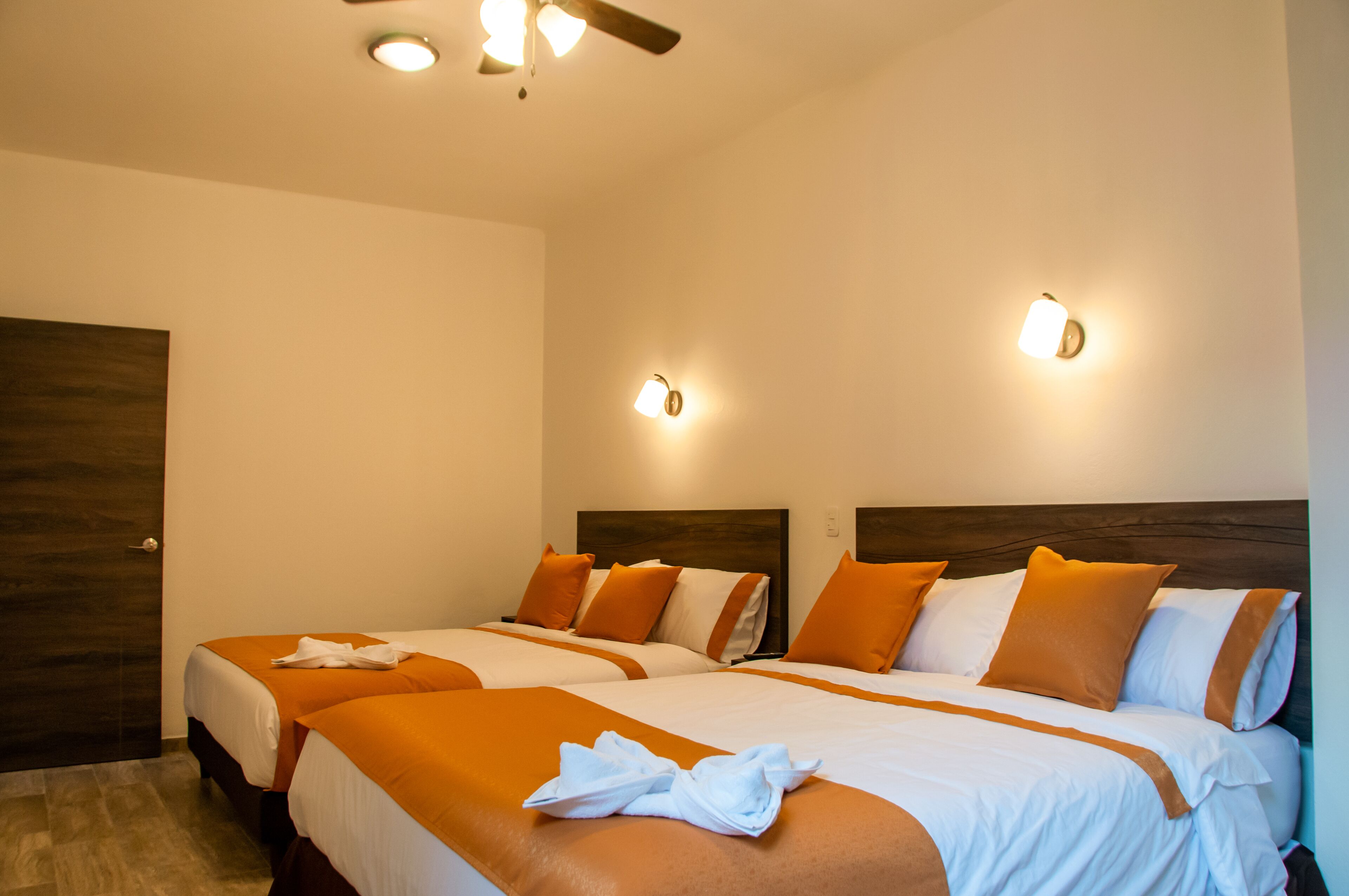 A hotel room with two beds, each with orange bedding and white pillows, a wooden headboard, and a ceiling fan.
