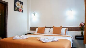 Une chambre d’hôtel avec un grand lit, deux lampes fixées au mur, un tableau et un vase rempli de fleurs.