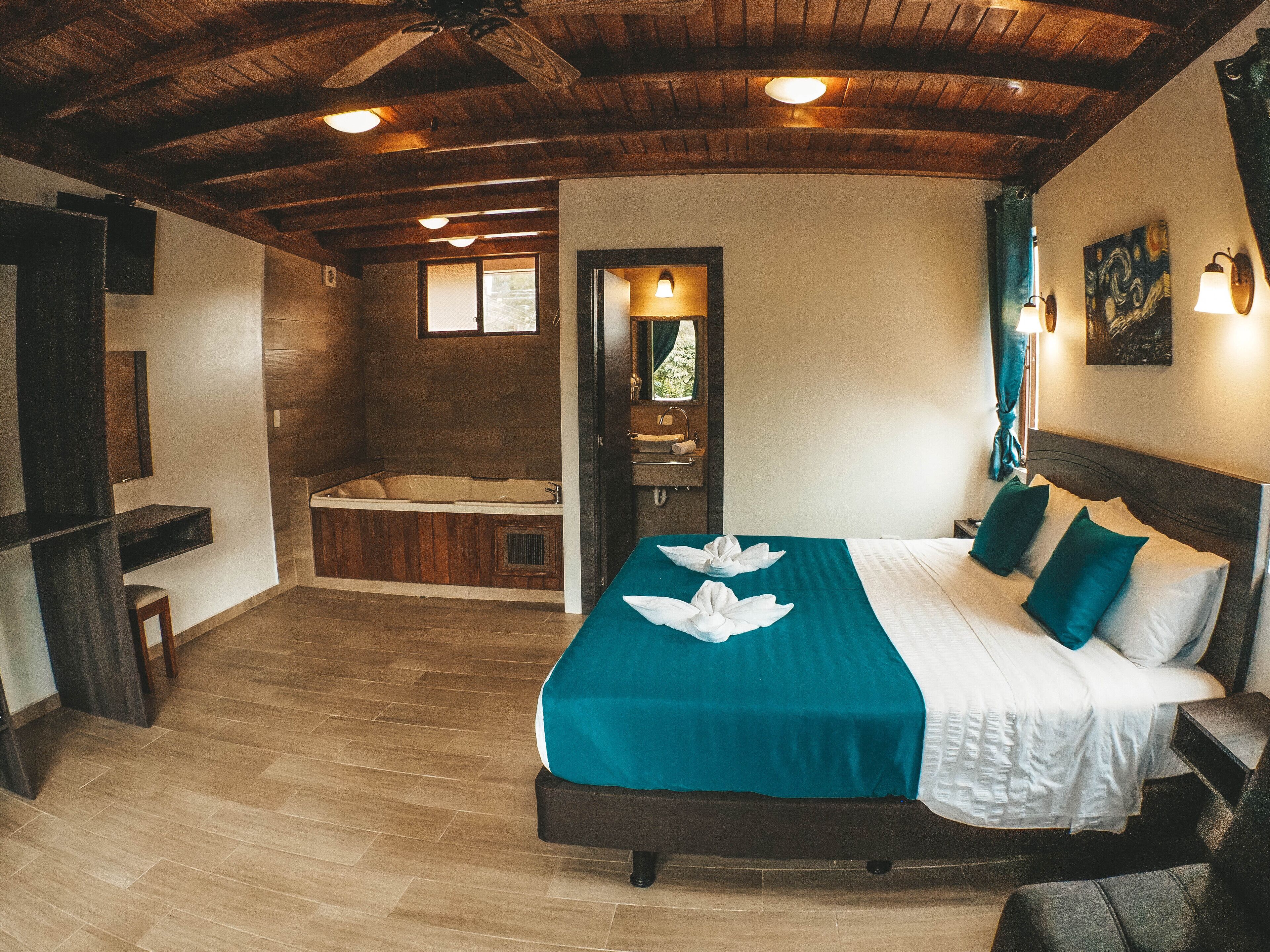 A bedroom with a large bed, a wooden ceiling, a bathtub, and a small window.