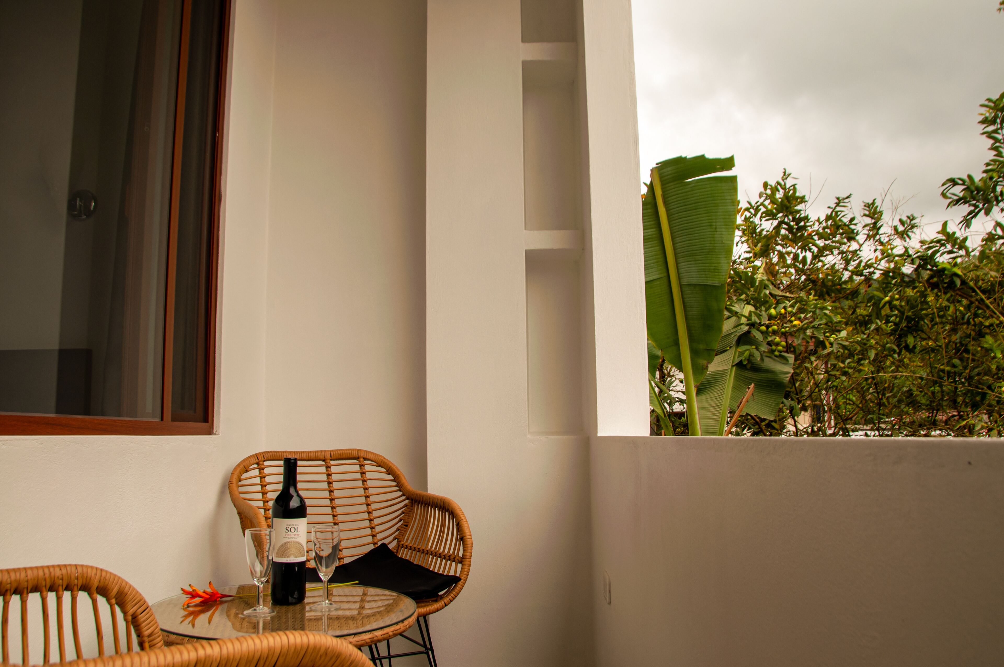 A balcony with wicker chairs, a table with a bottle of wine, and a view of greenery.
