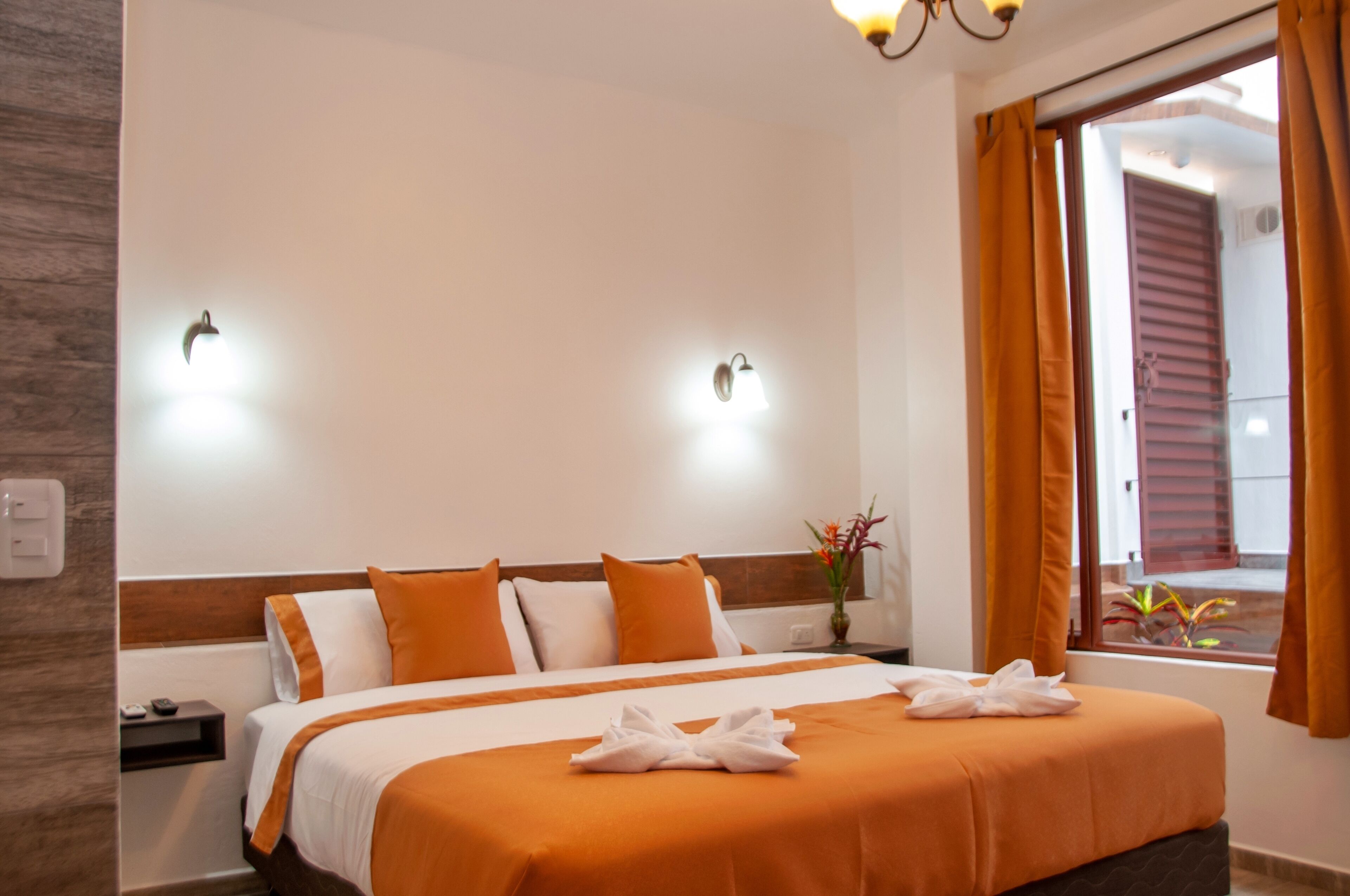 Habitación de hotel con cama, dos lámparas de pared, una mesita de noche, una ventana con cortinas y vistas al exterior.