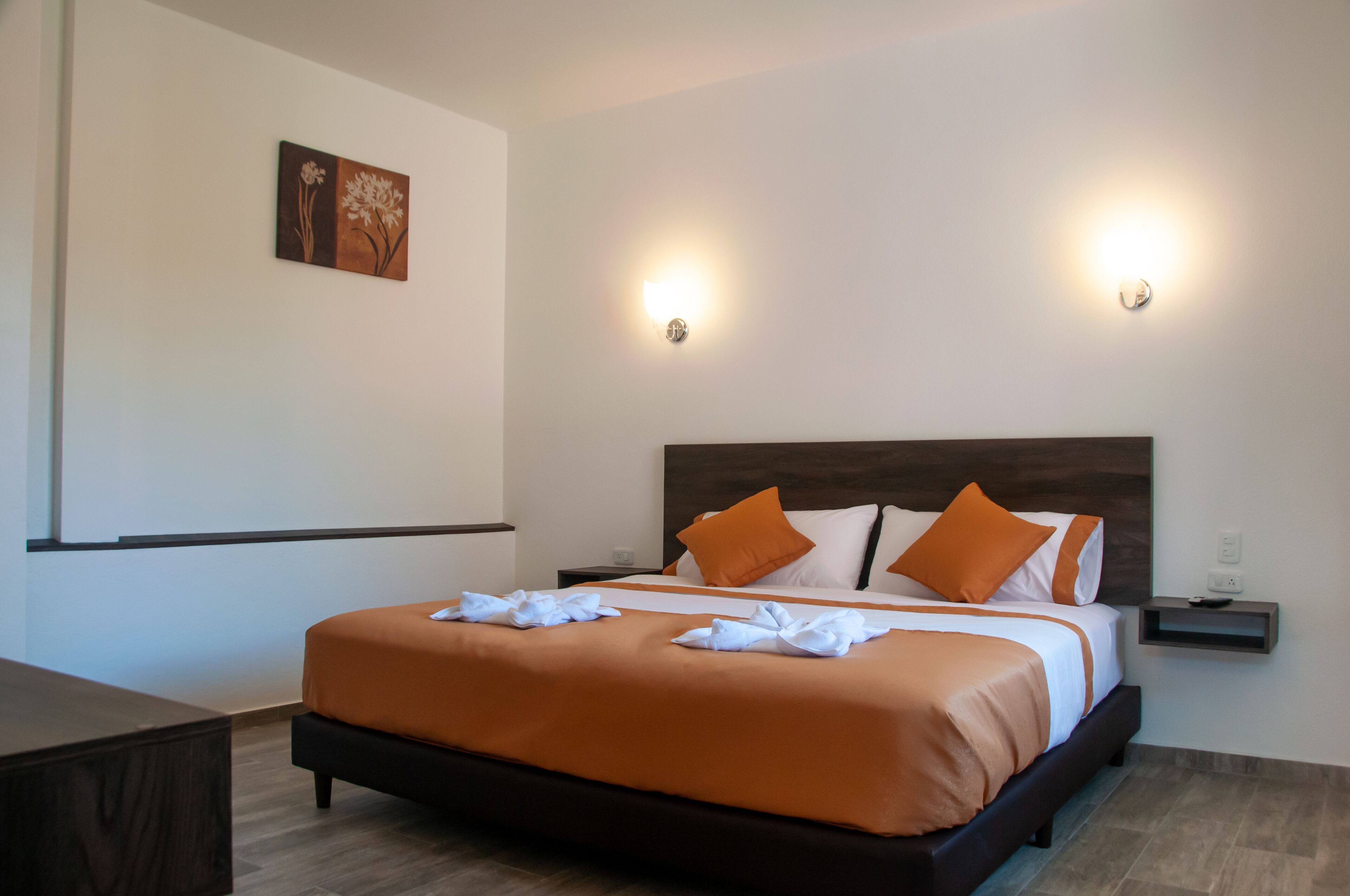 Une chambre d’hôtel avec un grand lit, deux tables de chevet, une petite table et un luminaire fixé au mur.