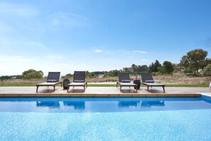 Un espace aménagé au bord de la piscine, comprenant quatre chaises longues et une terrasse en bois.