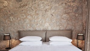 Een slaapkamer met een stenen muur, een bed met wit beddengoed en twee bedlampjes.