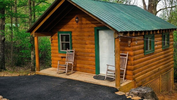 A small log cabin with a green roof, two wooden chairs outside, and a door. - Log Cabin in North Georgia Mountains (Dahlonega)